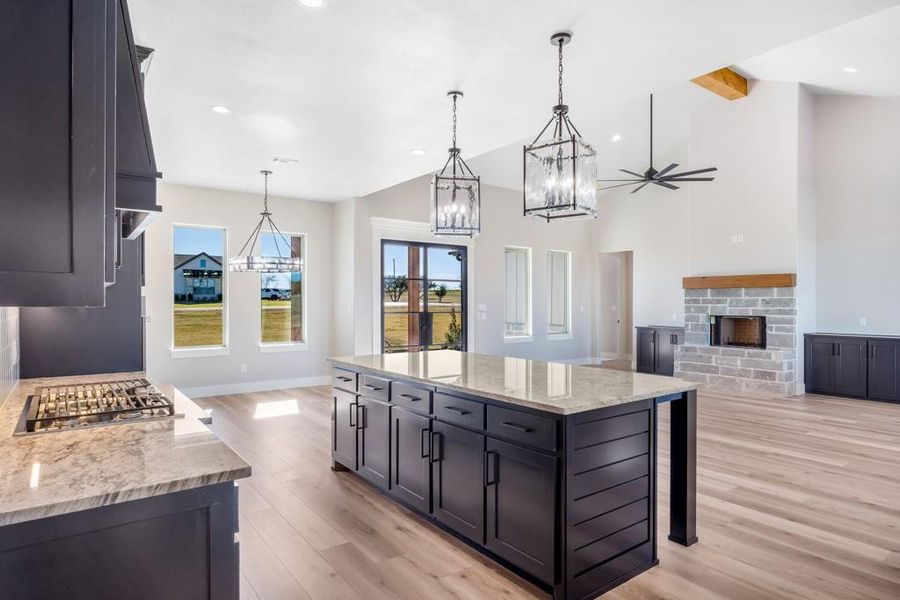 Kitchen with a large island, a fireplace, light stone countertops, and decorative light fixtures