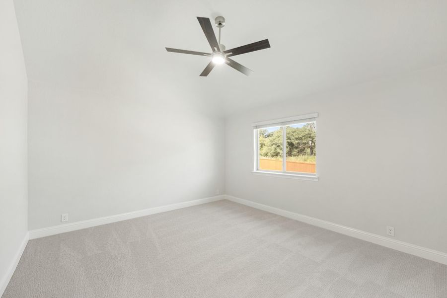 Empty bedroom with vaulted ceiling, ceiling fan, carpet flooring, and a single window with backyard view
