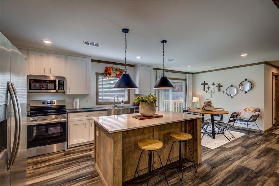 Kitchen featuring appliances with stainless steel finishes, white cabinetry, a breakfast bar area, dark wood-style floors, and ornamental molding