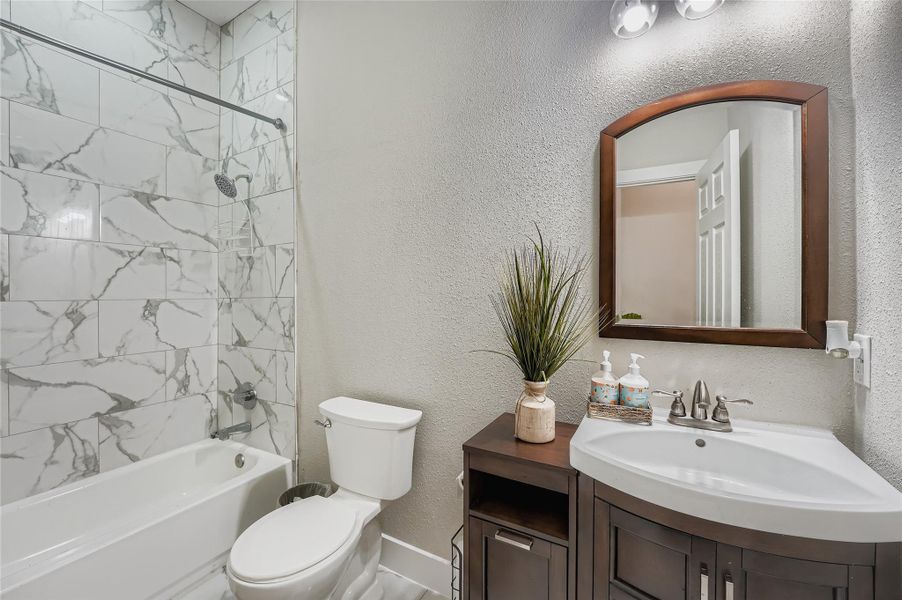 Bathroom featuring bathtub / shower combination, vanity, and a textured wall Bathroom featuring bathtub / shower combination, vanity, and a textured wall