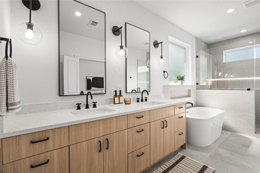 This view shows the large primary vanity with its double-sink layout and white quartz countertop. Warm wood cabinets with black hardware provide plenty of storage, while two large black-framed mirrors and glass globe sconces create a bright, functional space.