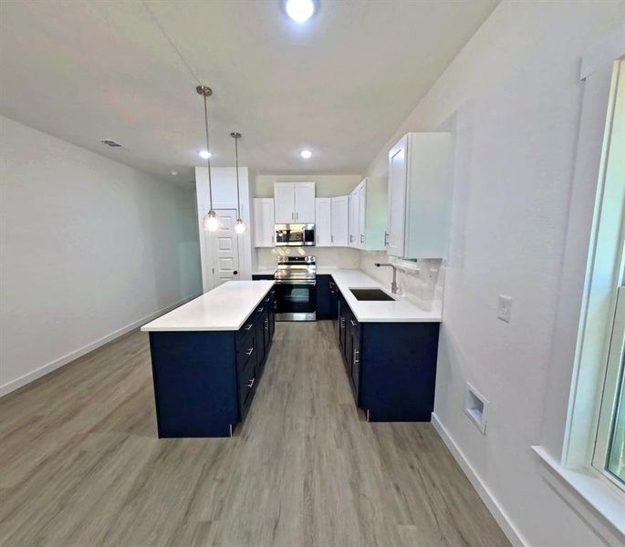 Kitchen featuring white cabinets, stainless steel appliances, dark cabinetry, light wood-style flooring, and decorative light fixtures Kitchen featuring white cabinets, stainless steel appliances, dark cabinetry, light wood-style flooring, and decorative light fixtures