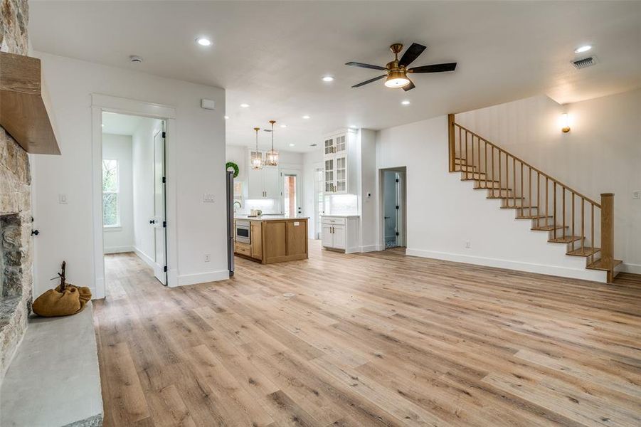 Unfurnished living room with ceiling fan with notable chandelier, a stone fireplace, and light hardwood / wood-style flooring