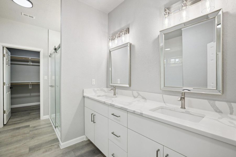 Full bathroom featuring double vanity, a shower stall, a spacious closet, and light wood-type laminate flooring
