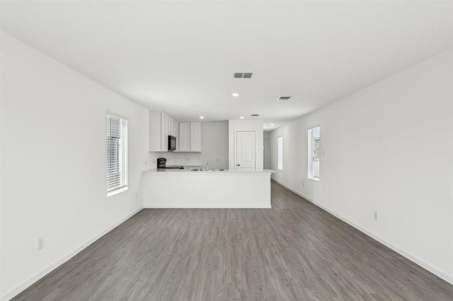 Open-concept living area featuring wood-finish flooring, white walls, recessed lighting, and a kitchen with white cabinetry
