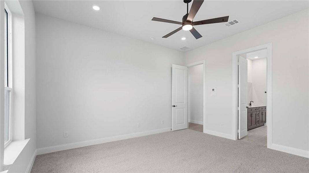 Spacious room featuring light gray carpet flooring, white walls, and a dark-toned ceiling fan with integrated lighting