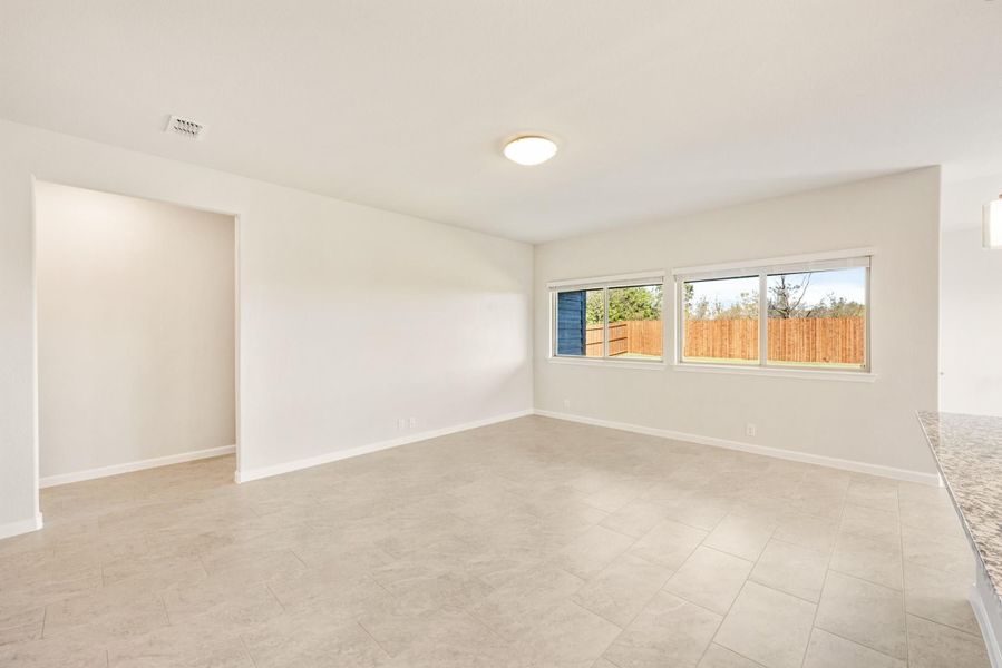 Empty living room with tile floors, white walls, and a large window overlooking a fenced backyard