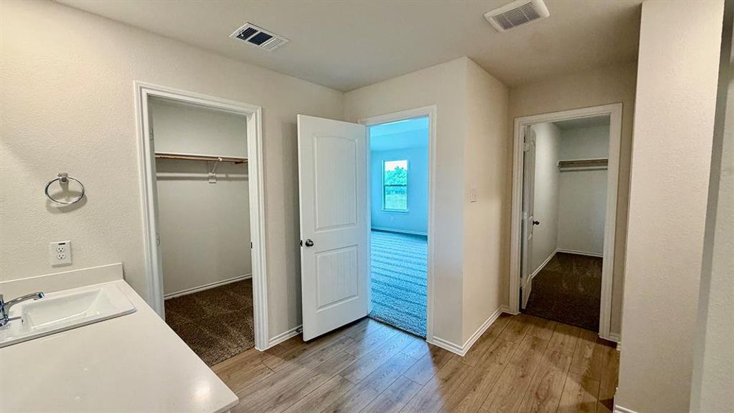 Hallway with wood-finish flooring, featuring a built-in vanity with an undermount sink and chrome faucet, and two separate closet entries with carpet flooring and clothing rods