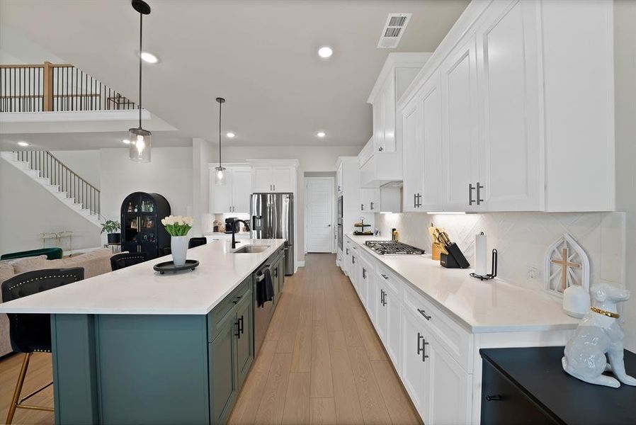 Open-concept kitchen featuring an expansive central island with a sink, white perimeter cabinetry, and light wood-finish flooring Open-concept kitchen featuring an expansive central island with a sink, white perimeter cabinetry, and light wood-finish flooring