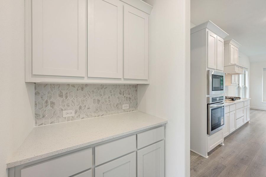 Kitchen with white cabinets, quartz countertops, hexagon tile backsplash, and stainless steel double oven