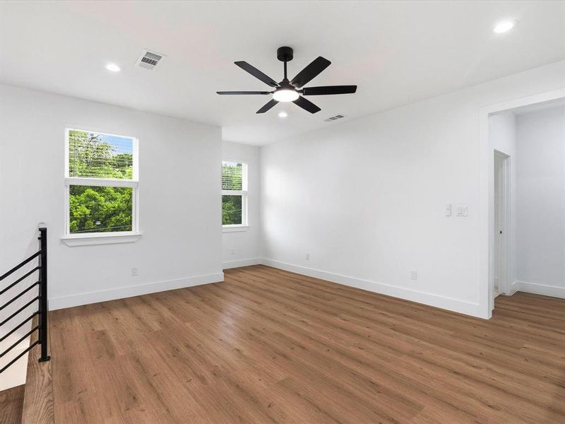 Spacious room featuring wood-finish flooring, multiple windows, a ceiling fan with integrated lighting, and recessed lighting