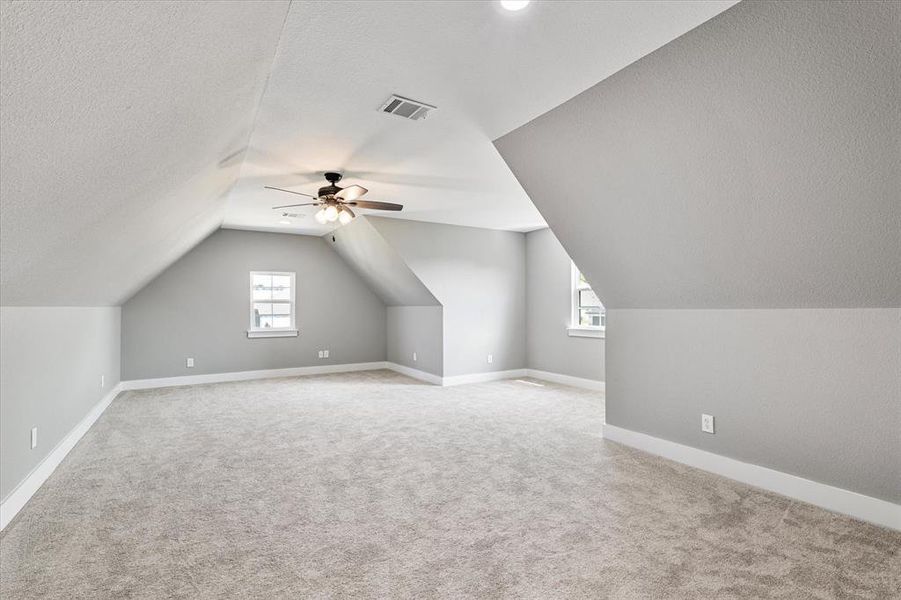 Bonus room with ceiling fan, vaulted ceiling, light colored carpet, and a textured ceiling