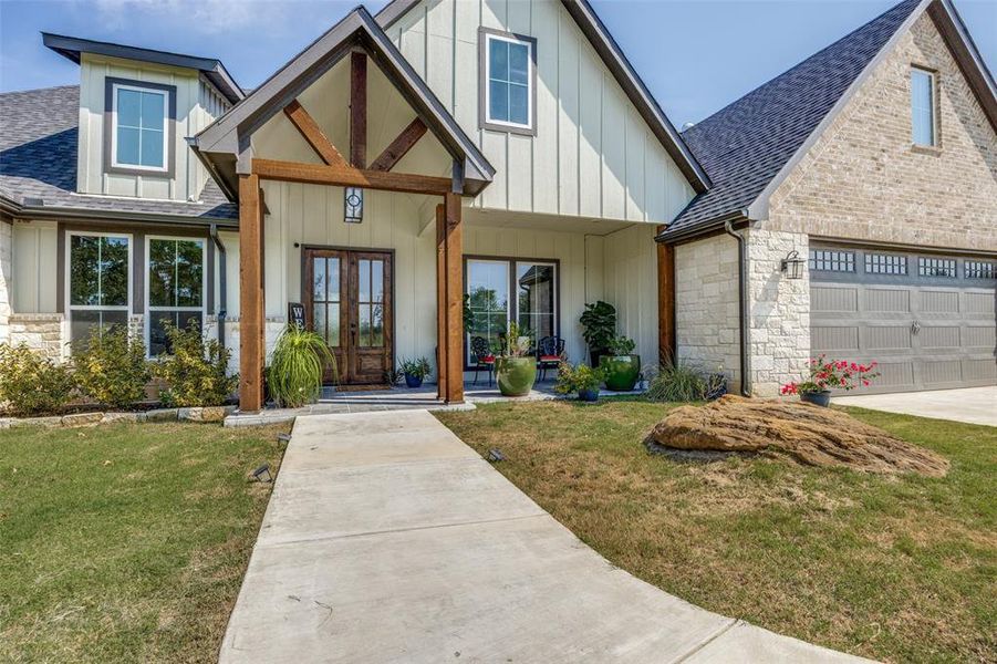 View of front of house with a shingled roof, covered porch, stone siding, and french doors