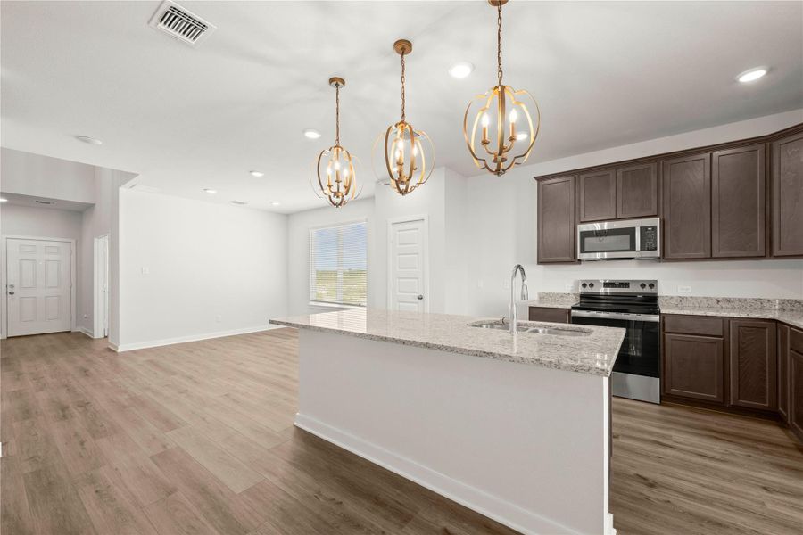 An open-concept living space features a functional kitchen island and warm wood-look flooring.