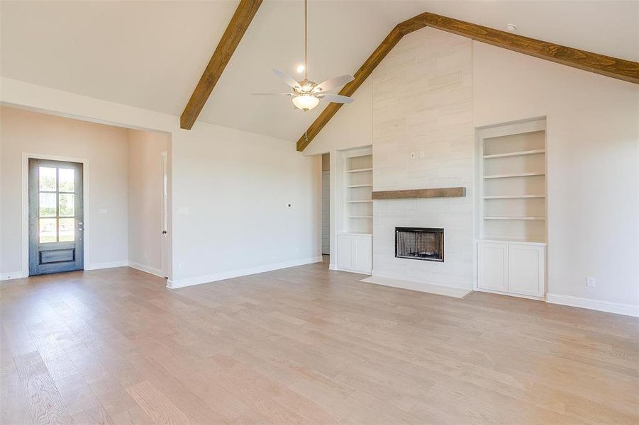 Unfurnished living room featuring beam ceiling, light hardwood / wood-style flooring, built in features, a fireplace, and high vaulted ceiling