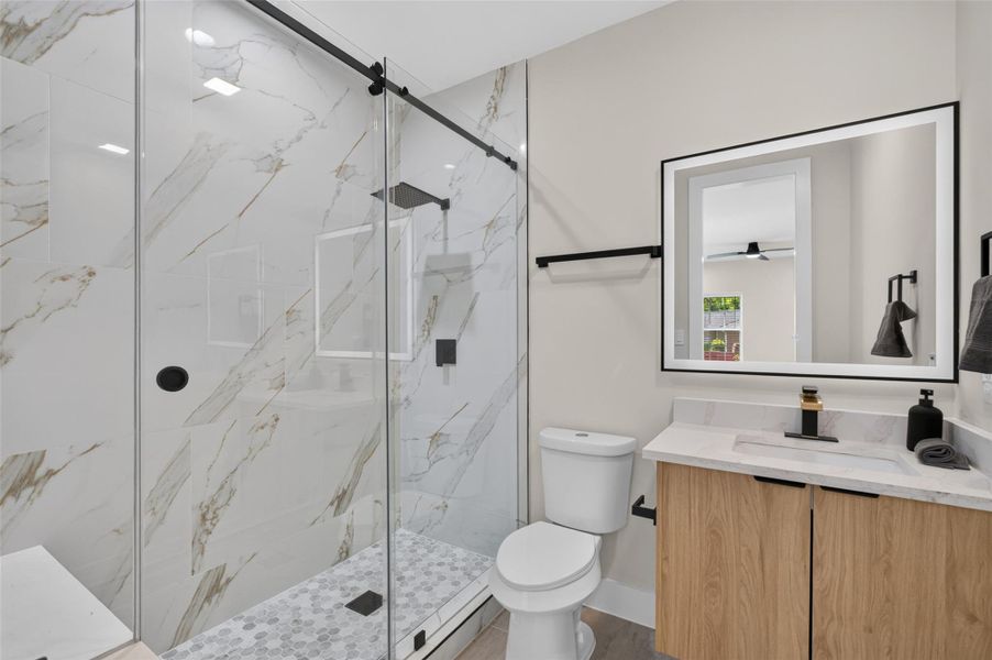 Elegant bathroom featuring a spacious glass-enclosed shower with marble-patterned tiles, a sleek vanity with modern fixtures, and a stylish backlit mirror.