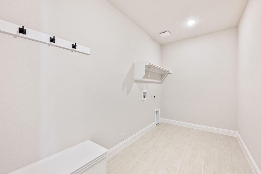 Laundry room with white walls, tile floor, wall-mounted shelf, coat hooks, and washer and dryer hookups Laundry room with white walls, tile floor, wall-mounted shelf, coat hooks, and washer and dryer hookups