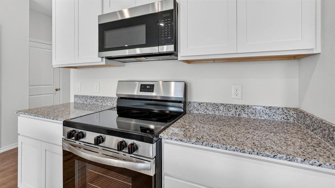 Kitchen featuring granite countertops, white cabinetry, stainless steel range, and an over-the-range microwave Kitchen featuring granite countertops, white cabinetry, stainless steel range, and an over-the-range microwave