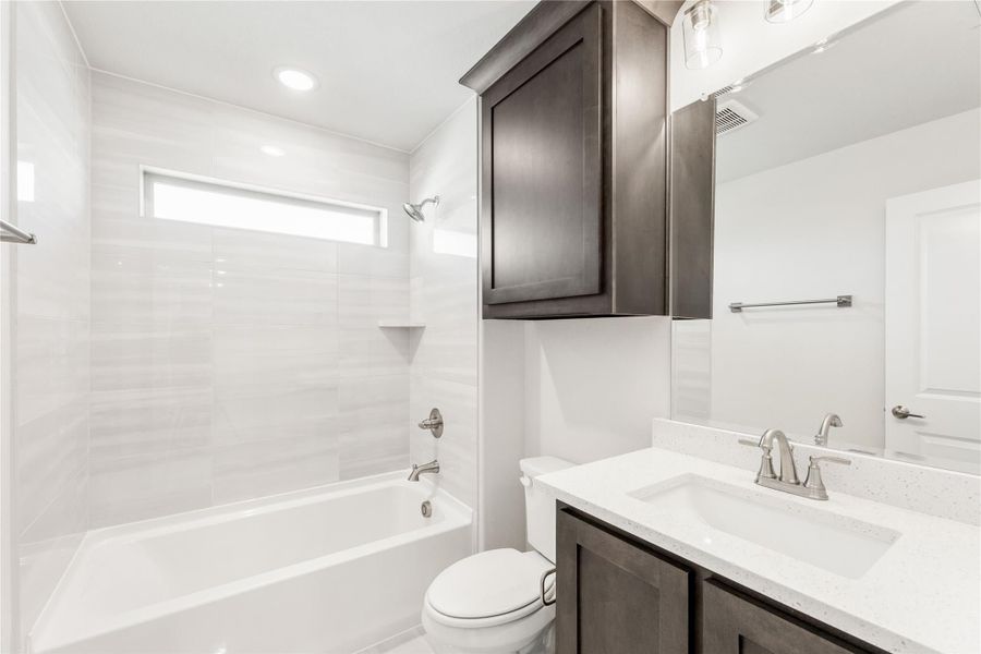 Bathroom with tiled tub-shower combo, dark wood vanity, white countertop, and large mirror Bathroom with tiled tub-shower combo, dark wood vanity, white countertop, and large mirror