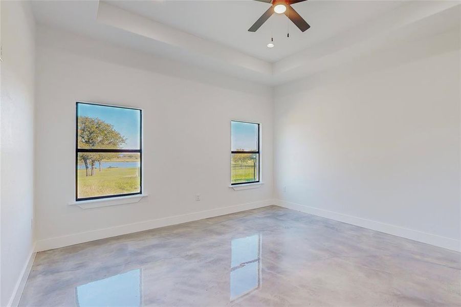 Empty room featuring a raised ceiling, ceiling fan, and plenty of natural light