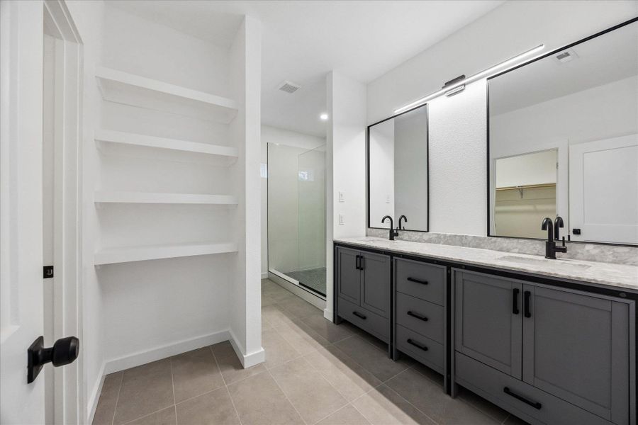 Modern primary bathroom offers dual vanities with elegant black fixtures and a sleek glass-enclosed shower.