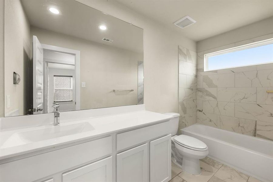 Secondary bathroom features light countertops and cabinets, custom paint, shower/tub combo with tile surround, large mirror, tile floors, sleek fixtures and modern finishes, plenty of space to accommodate any visiting family or guests.