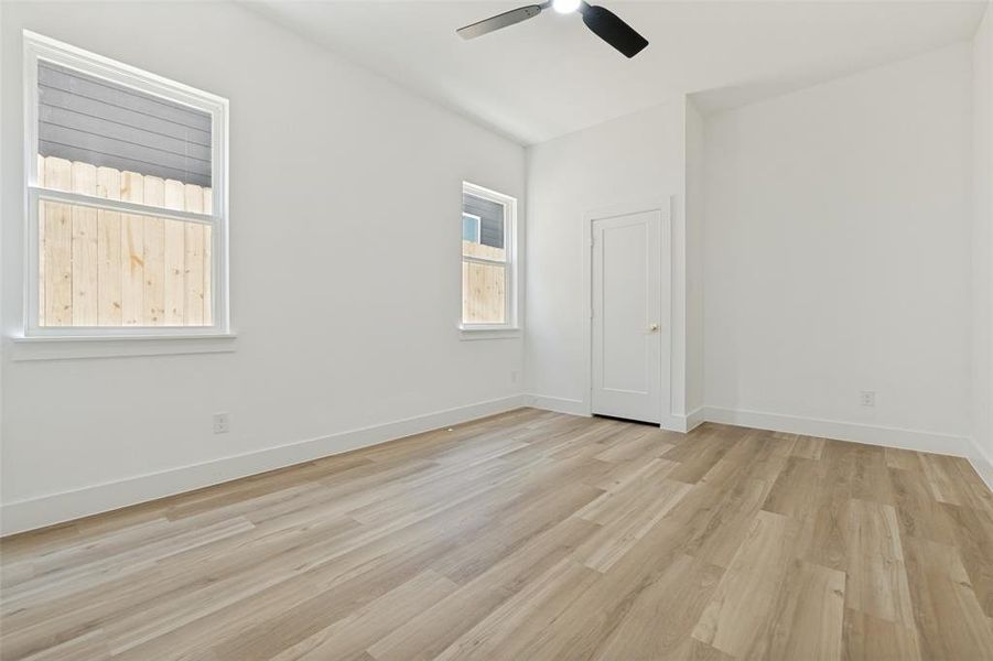 Spacious room featuring wood-finish flooring, white walls, and a ceiling fan Spacious room featuring wood-finish flooring, white walls, and a ceiling fan