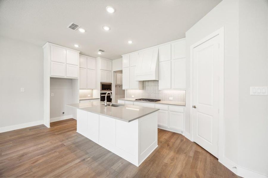 Kitchen with white cabinets, light hardwood / wood-style floors, a center island with sink, and custom exhaust hood