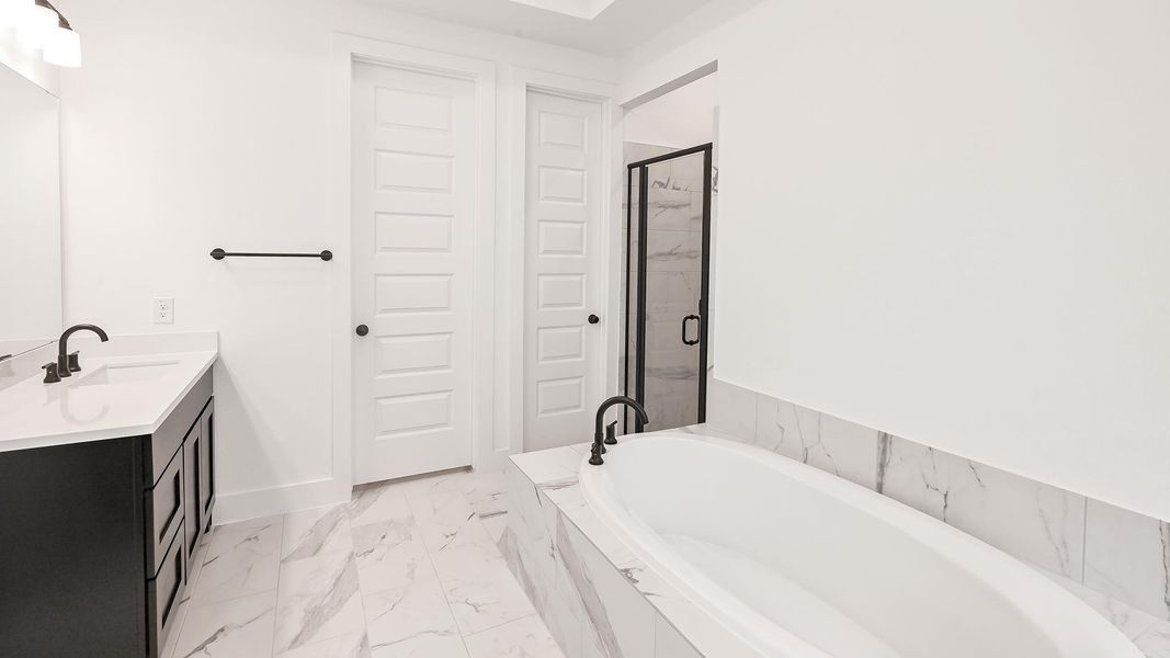 Bathroom with marble finish flooring, a bath, a stall shower, vanity, and baseboards Bathroom with marble finish flooring, a bath, a stall shower, vanity, and baseboards
