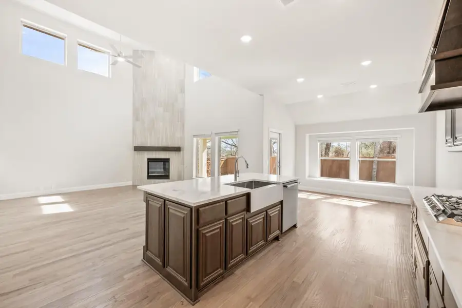 Open-concept kitchen with dark wood island, white countertops, and vaulted ceiling open to living area with fireplace