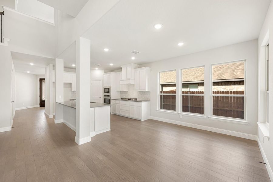 Open-concept living area and kitchen with white cabinets, wood floors, and large windows