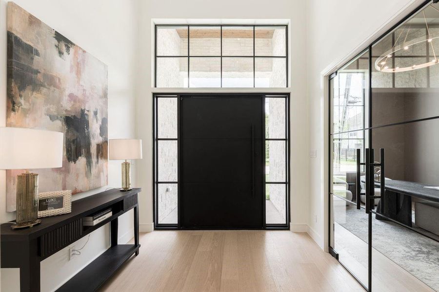 A soaring two-story foyer makes an unforgettable first impression, where steel-framed glass and sculptural lighting set a tone of quiet drama. Sunlight spills across warm oak floors, guiding you into a home designed for both statement and serenity.
