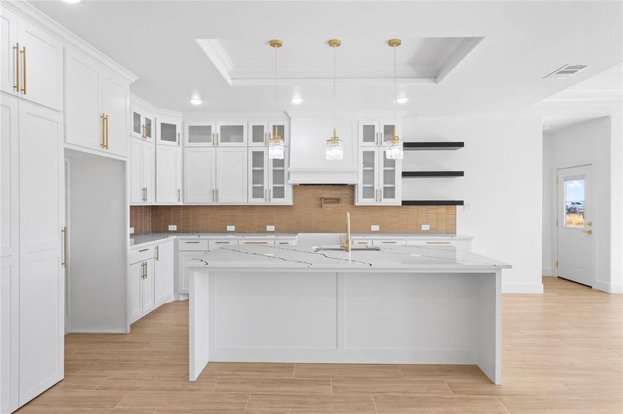 Kitchen featuring a tray ceiling, decorative backsplash, white cabinetry, glass insert cabinets, and wood finish floors Kitchen featuring a tray ceiling, decorative backsplash, white cabinetry, glass insert cabinets, and wood finish floors
