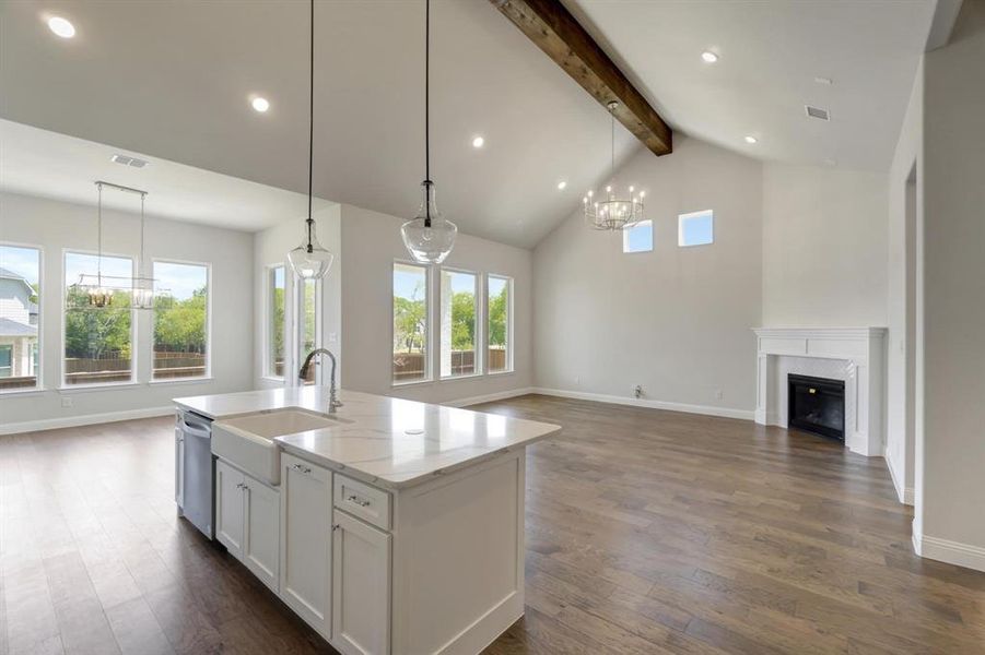 Kitchen with a notable chandelier, an island with sink, sink, a high end fireplace, and dark wood-type flooring