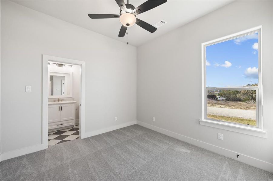 Unfurnished bedroom with a ceiling fan, light carpet, and ensuite bath