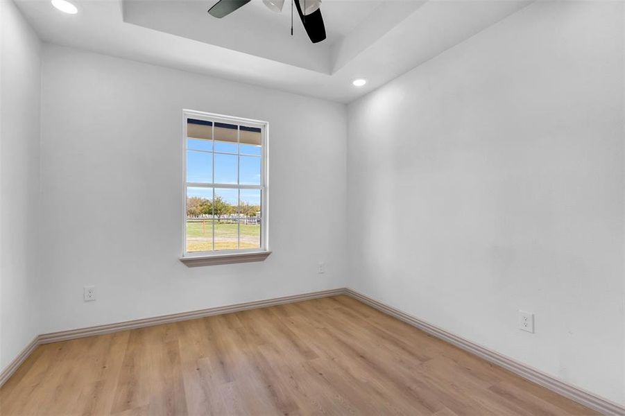 Unfurnished room featuring a raised ceiling, light hardwood / wood-style flooring, and ceiling fan