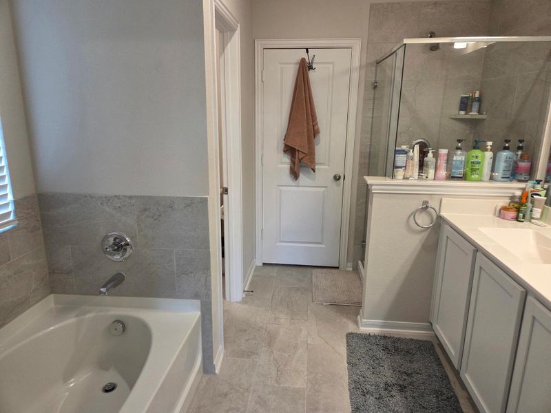 Bathroom featuring a built-in tub with tile surround, a glass-enclosed shower, a double vanity with an undermount sink, light-colored cabinetry, and tile flooring