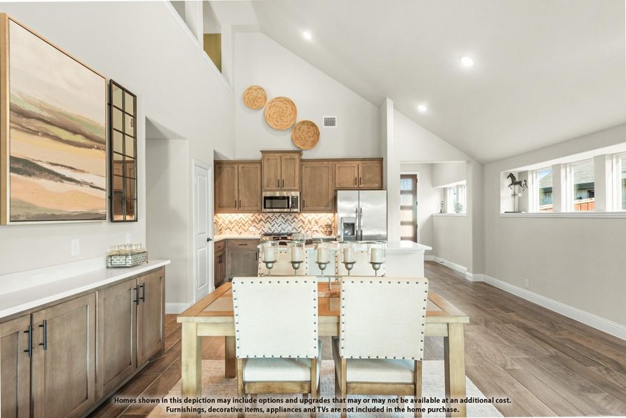 Open dining area with wood table flowing into kitchen with brown cabinets, tile backsplash, and vaulted ceiling Open dining area with wood table flowing into kitchen with brown cabinets, tile backsplash, and vaulted ceiling