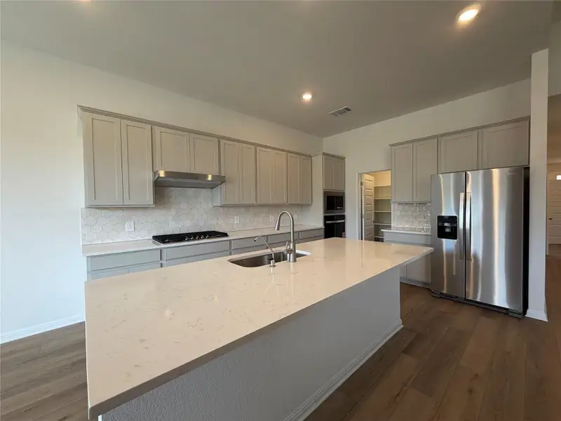 Kitchen featuring decorative backsplash, appliances with stainless steel finishes, dark wood-style floors, gray cabinetry, and an island with sink