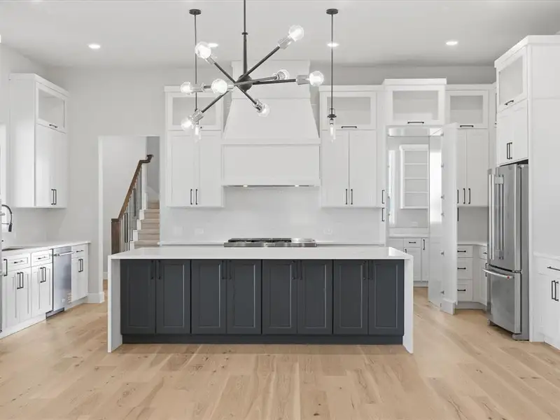Spacious kitchen featuring a central island with dark cabinetry, white perimeter cabinetry, and light wood-finish flooring