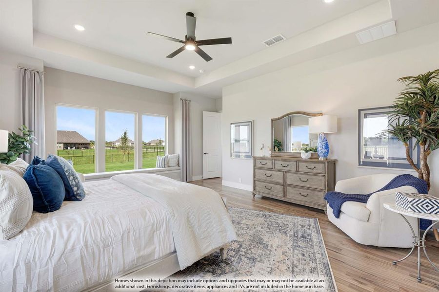 Spacious master bedroom with tray ceiling, ceiling fan, hardwood floors, and large windows with backyard views