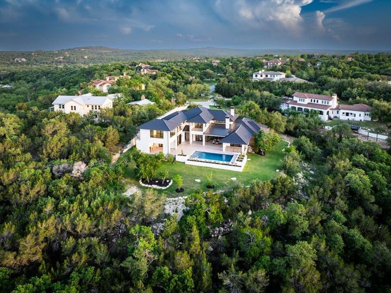 This property features a contemporary design with a dark-tiled roof and white exterior, set within a lush, green landscape