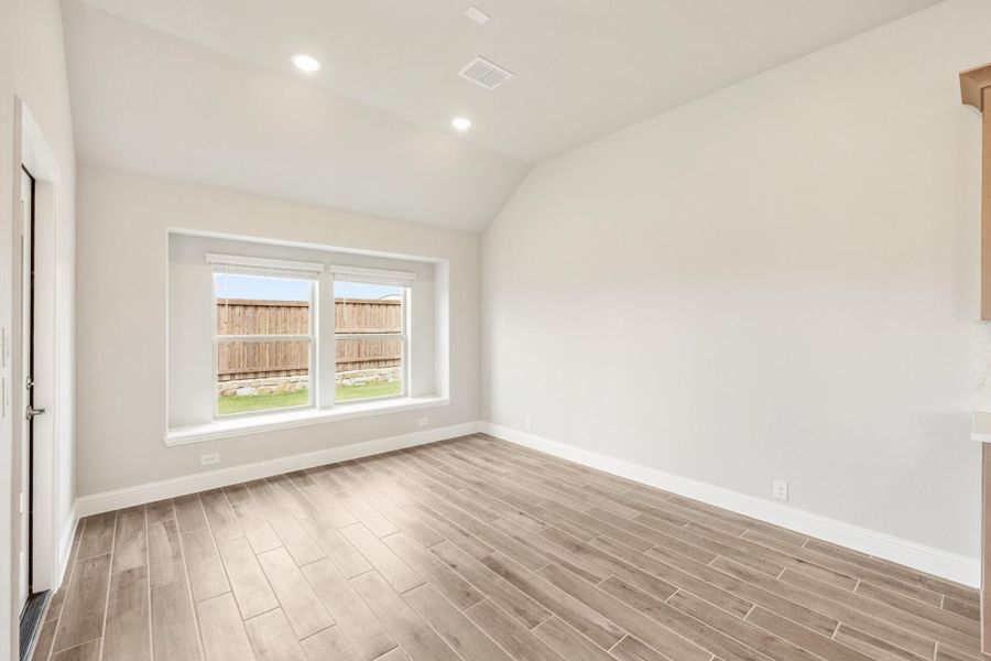 Empty room with vaulted ceiling, wood-look tile floors, and a backyard-facing window
