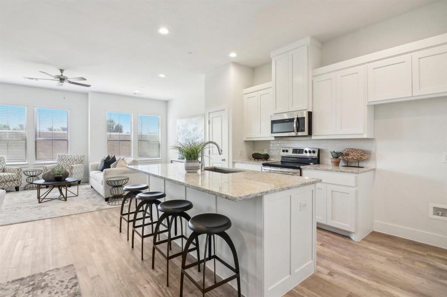 Kitchen featuring appliances with stainless steel finishes, ceiling fan, sink, a center island with sink, and white cabinets