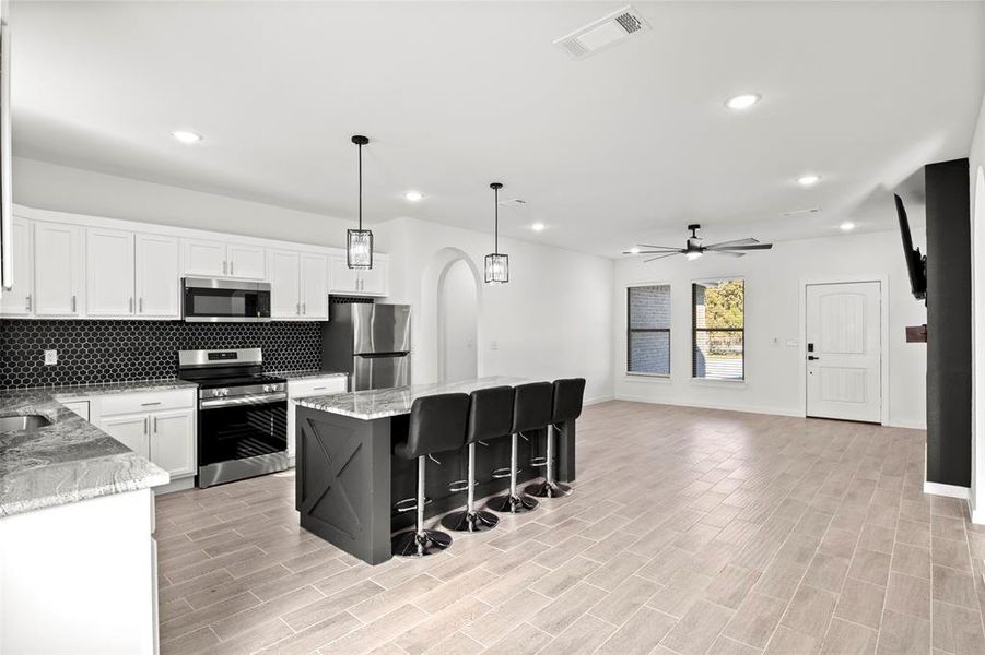 Kitchen with white cabinets, stainless steel appliances, decorative backsplash, hanging light fixtures, and a kitchen island