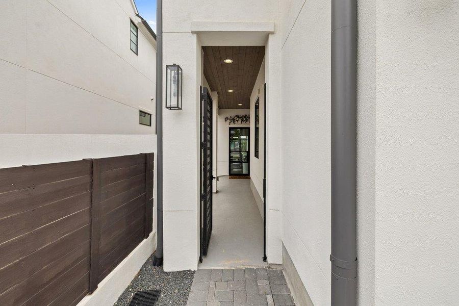 Entryway featuring a decorative metal gate, exposed aggregate paving stones, and a contemporary exterior sconce