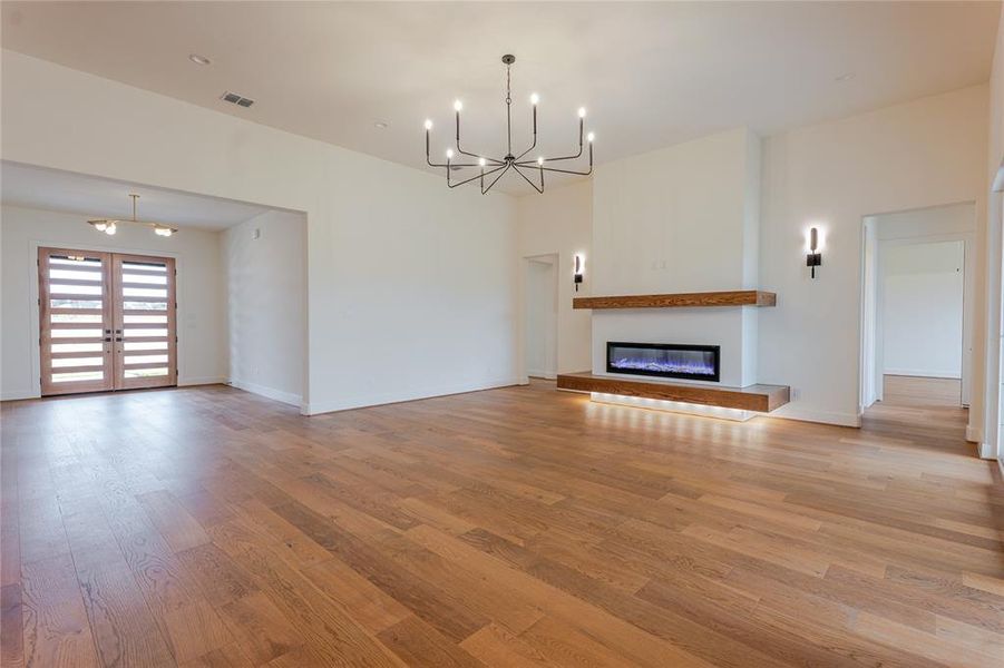 Unfurnished living room with a chandelier, a glass covered fireplace, light wood-style floors, and french doors