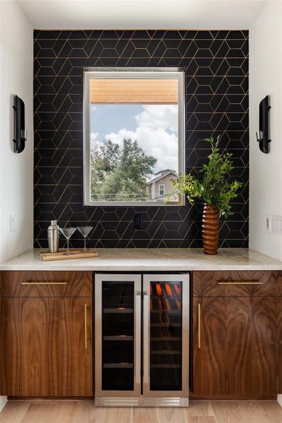 The wet bar area is enhanced with a stylish tile backsplash and features a convenient drink fridge, creating an elegant space for mixing and serving beverages.