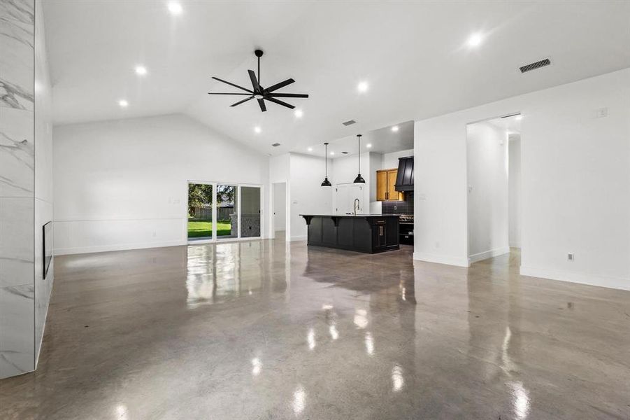 Unfurnished living room featuring finished concrete flooring, ceiling fan, high vaulted ceiling, and recessed lighting