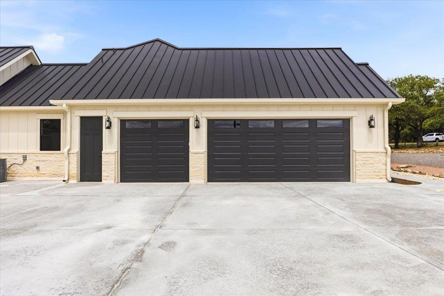 A sleek metal roof tops this contemporary home, featuring twin garage doors and natural stone accents.
